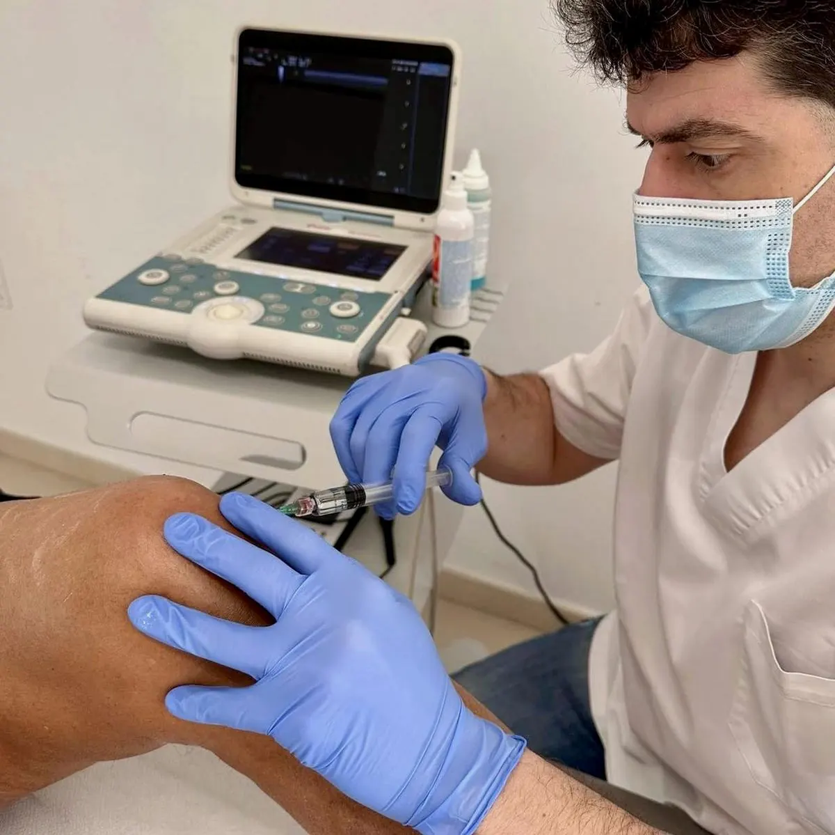 El Dr. Enrique Martínez, con mascarilla y guantes, haciendo una ecografía junto al ecógrafo